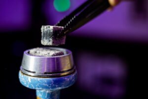 Hete shisha kool met as wordt met een tang op de waterpijp-kop geplaatst.