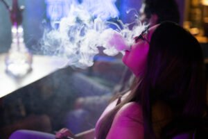Vrouw blaast rook uit shisha (hookah) in sfeervolle, donkere bar.